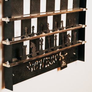 May include: A black wooden chessboard wall shelf with a white and black checkerboard pattern. The shelf has two tiers and is decorated with black chess pieces. The shelf is labeled "Chess" in a stylized font.