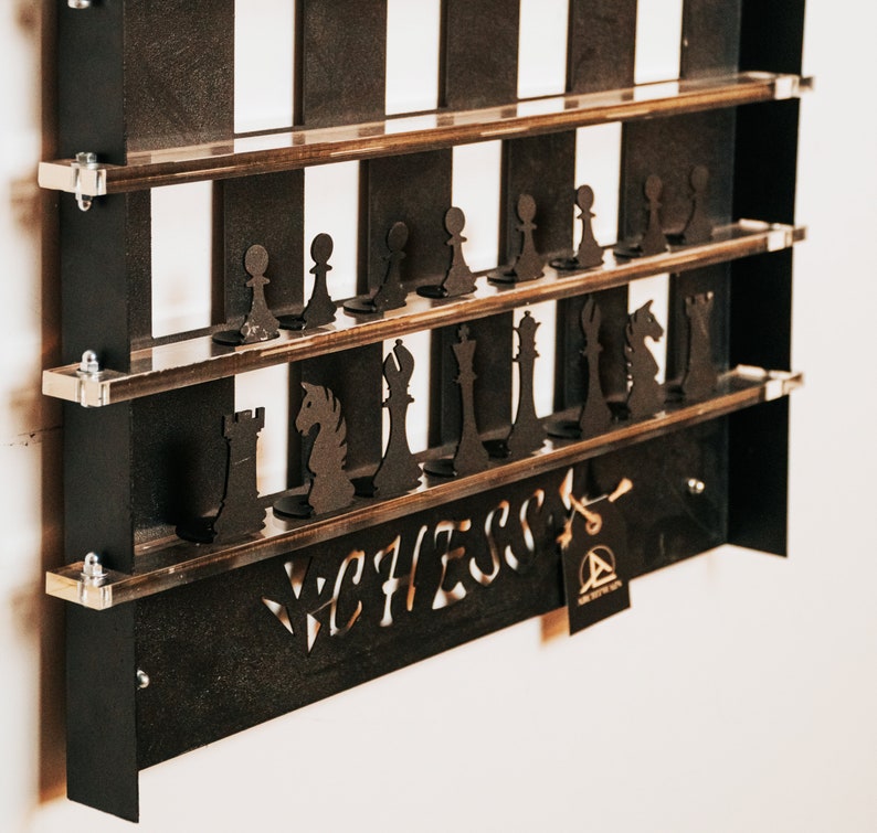 May include: A black wooden chessboard wall shelf with a white and black checkerboard pattern. The shelf has two tiers and is decorated with black chess pieces. The shelf is labeled "Chess" in a stylized font.