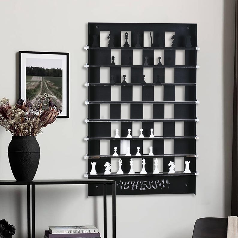 May include: Black wall-mounted chessboard with white and black squares. The chessboard has shelves for storing chess pieces. The chess pieces are white and black plastic. The chessboard has the word "CHESS" written on the bottom.
