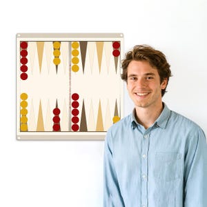 Puede incluir: Un tablero de backgammon rectangular con fondo beige y borde beige. El tablero presenta triángulos marrones y beige alternados, con fichas rojas y amarillas. El tablero está colgado en una pared blanca.