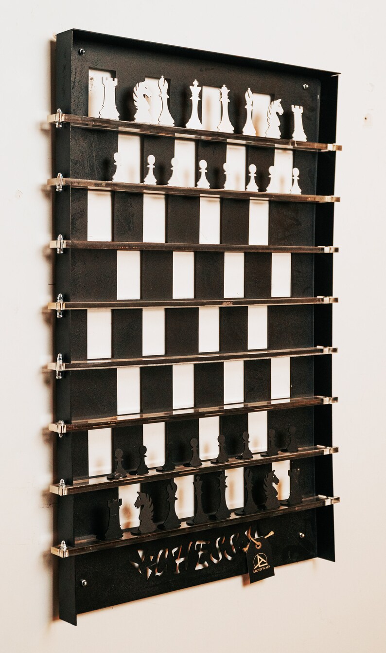 May include: A black metal wall-mounted chessboard with white and black squares. The chess pieces are made of wood and are displayed on shelves. The board is labeled "Chess" and has a small tag with the logo "Architects of Fun".