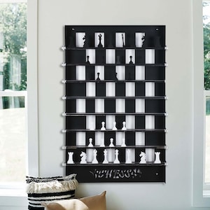 May include: A black wall-mounted chessboard with white squares and black squares. The chessboard has a shelf for each square and is designed to hold chess pieces. The chessboard has the word "CHESS" written on the bottom.
