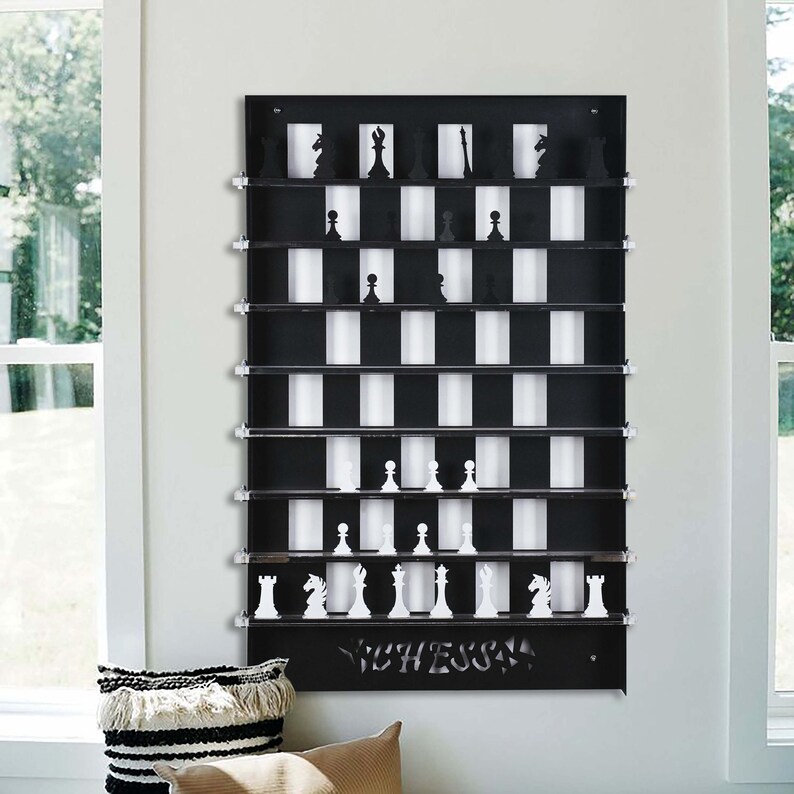 May include: A black wall-mounted chessboard with white squares and black squares. The chessboard has a shelf for each square and is designed to hold chess pieces. The chessboard has the word "CHESS" written on the bottom.