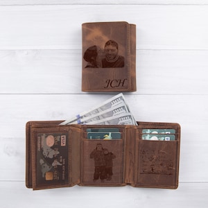 Puede incluir: Cartera de cuero marr&oacute;n de tres pliegues con una foto de una pareja grabada en la parte delantera. La cartera tiene m&uacute;ltiples ranuras para tarjetas y un clip para billetes. El texto "JCH" tambi&eacute;n est&aacute; grabado en la parte delantera.