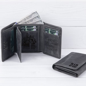 May include: Two gray leather wallets with a personalized inscription. One wallet has a photo of a family engraved on the front. The other wallet has the word "Dad" engraved on the front.