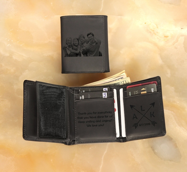 May include: Black leather trifold wallet with a personalized message and a photo of a family engraved on the front. The message reads "Thank you for everything that you have done for us! Keep smiling and singing!! We love you!" and the initials "LAK" with a date.