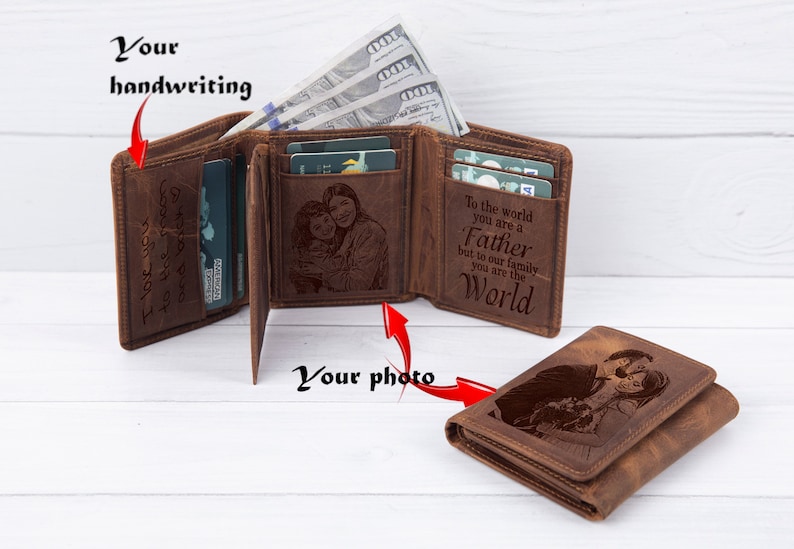 May include: A brown leather trifold wallet with a personalized message and a photo engraved on the front. The message reads "To the world you are a Father but to our family you are the World".