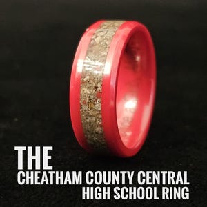 May include: A red ring with a band of light-coloured material. The ring has the text "THE CHEATHAM COUNTY CENTRAL HIGH SCHOOL RING" in white.