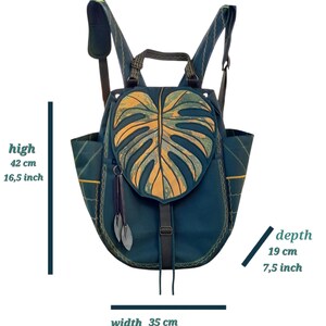 May include: A dark teal backpack featuring a large monstera leaf-shaped flap in yellow and green. It has adjustable shoulder straps, side pockets, and two leaf-shaped zipper pulls. Dimensions are 16.5 inches high, 13.7 inches wide, and 7.5 inches deep.