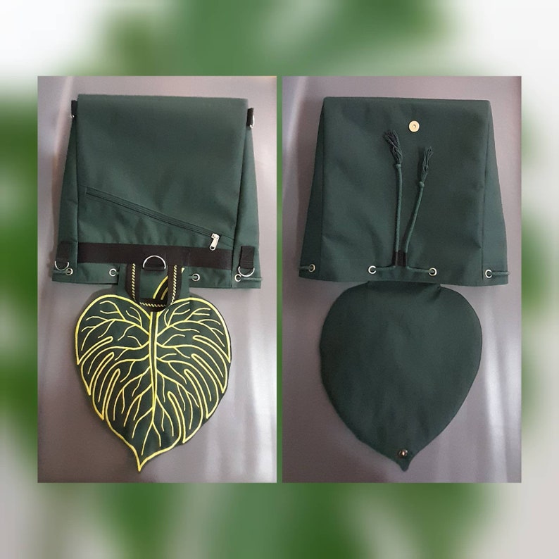 May include: A dark green backpack featuring a large, heart-shaped leaf flap with yellow embroidered veins. The bag includes a black horizontal strap, metal D-rings, a diagonal zippered pocket, and a drawstring closure with a magnetic snap button.