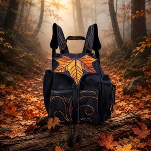 Può includere: Uno zaino blu navy scuro caratterizzato da un grande disegno di una foglia d'acero arancione e gialla sulla patta anteriore. La borsa include una tasca frontale con motivi a linee arancioni a spirale, spallacci regolabili e un piccolo ciondolo a forma di foglia.