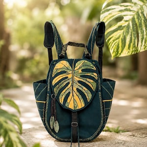 Monstera Aurea Variegata convertible backpack photographed in soft natural light, surrounded by lush botanical greenery with a dreamy blurred background. A handcrafted statement piece inspired by rare tropical plants and designed for nature lovers with an artistic soul.