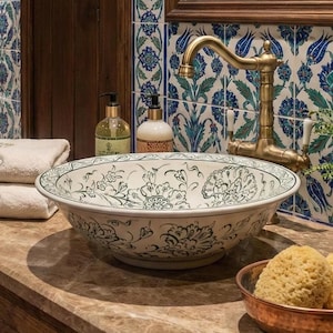 May include: A bathroom interior with a patterned ceramic sink, brass tap, and matching towels. The sink is on a wooden vanity with a marble surface. The walls are decorated with patterned tiles and a mirror, creating a luxurious feel.