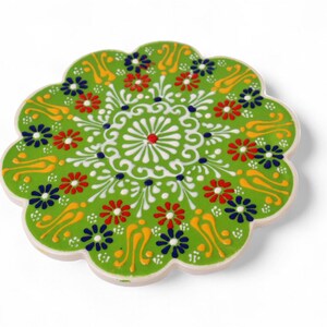 Puede incluir: Posavasos de cerámica verde con un diseño floral blanco y colorido. El posavasos tiene un borde festoneado y es perfecto para proteger las superficies del calor.