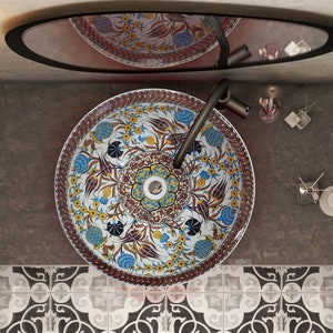 May include: Overhead view of a bathroom sink with a decorative floral pattern. The sink is round with a dark faucet. The countertop is dark gray, and the floor has a patterned tile design. A mirror is above the sink.