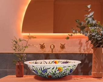Könnte beinhalten: Ein weißes Keramikwaschbecken mit floralem Muster steht auf einer Holztheke in einem Badezimmer. Das Waschbecken ist rund und hat einen breiten Rand. Das Blumenmuster ist bunt und zeigt blaue, grüne, gelbe und violette Blumen. Die Arbeitsplatte ist aus Holz und hat eine natürliche Oberfläche. Das Badezimmer ist modern eingerichtet mit rosa Wänden und einem grauen Fliesenboden.