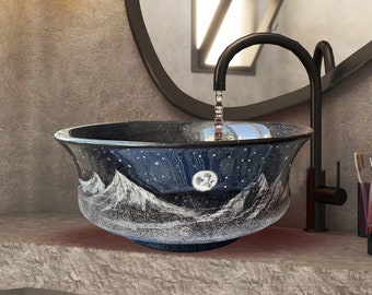 May include: A decorative bathroom sink with a mountain and starry night design. The sink is blue with white mountain peaks and a full moon. A black faucet is above the sink, and a mirror is behind it. The sink is on a gray stone counter.
