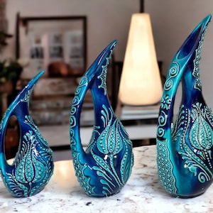 Könnte beinhalten: Drei blaue und grüne Keramikvasen mit aufwendigen floralen Designs. Die Vasen sind in verschiedenen Größen und in einer Reihe auf einer weißen Oberfläche angeordnet.