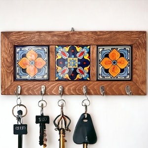 May include: A wooden key rack with three colorful ceramic tiles featuring floral designs. The rack has six hooks for hanging keys.