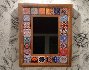 May include: A bathroom vanity with a white porcelain sink and a silver faucet. The wall behind the sink is covered in white wallpaper with a black floral pattern. A wooden framed mirror with a colorful tile border hangs above the sink.