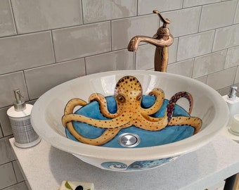May include: A white ceramic bathroom sink with a blue and white octopus design. The sink is on a white countertop with a bar of soap and a bottle of hand soap.
