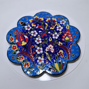 Puede incluir: Un posavasos de cerámica azul con un diseño floral. El diseño presenta flores rojas, blancas, amarillas y verdes sobre un fondo azul.