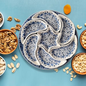 May include: A blue and white ceramic serving dish with six individual bowls. The bowls are arranged in a circular pattern and are perfect for serving snacks or appetizers. The dish is decorated with a floral design.