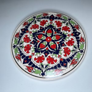 Puede incluir: Posavasos redondo de cerámica con fondo blanco y diseño floral azul, rojo y verde.