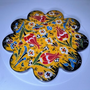 May include: A yellow ceramic coaster with a black outline and a floral design featuring red, white, and blue tulips and leaves.