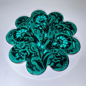 Puede incluir: Un diseño floral azul verdoso y negro sobre un fondo blanco. El diseño tiene la forma de una flor con múltiples pétalos.