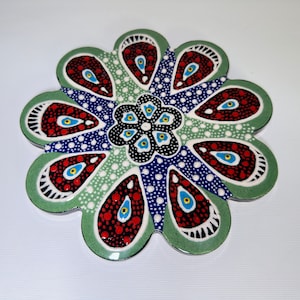 Puede incluir: Un azulejo de cerámica verde, azul, rojo y blanco con un diseño de flor. El azulejo está decorado con pequeños puntos y tiene un borde elevado.