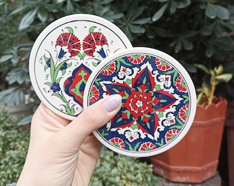 Puede incluir: Dos posavasos redondos de cerámica con intrincados diseños florales. Un posavasos presenta un patrón floral azul, rojo y verde con una estrella en el centro. El otro posavasos presenta un patrón floral rojo, azul y verde con una flor estilizada en el centro.