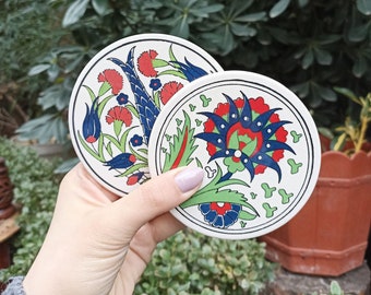 Puede incluir: Dos posavasos redondos de cerámica con intrincados diseños florales en azul, verde, rojo y blanco. Los posavasos presentan patrones tradicionales turcos.