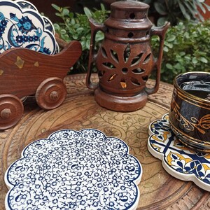 Może przedstawiać: Zestaw niebieskich i białych ceramicznych podkładek z misternymi wzorami kwiatowymi. Podkładki są umieszczone na drewnianej powierzchni z brązową ceramiczną latarnią i filiżanką herbaty.