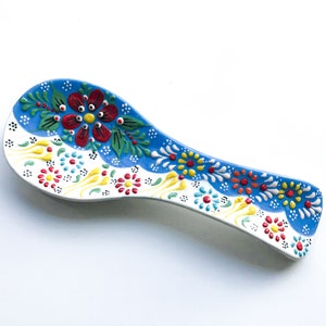 May include: A blue and white ceramic spoon rest with a floral design. The design features red, yellow, green, and blue flowers.