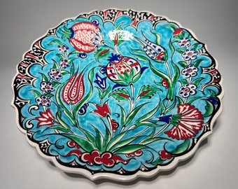 Puede incluir: Un plato redondo de cerámica con fondo azul y borde blanco. El plato está decorado con un patrón floral en rojo, blanco y verde.