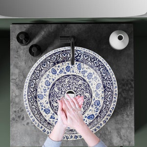 May include: A white ceramic sink with a blue and white floral pattern. The sink is round and has a small hole in the center. The sink is set on a gray countertop.