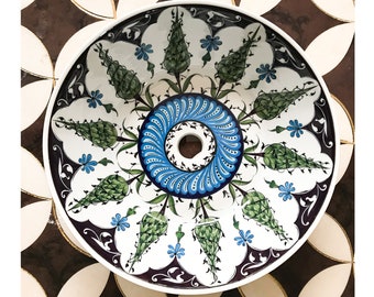 May include: A white ceramic sink with a blue and green floral design. The sink has a round shape and a drain hole in the center.