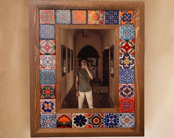 May include: A wooden framed mirror with a colourful mosaic tile design. The mirror reflects a person standing in a hallway.