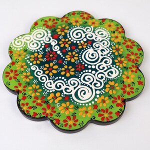 以下が含まれることがあります： 緑、白、赤、黄色の花柄と渦巻き模様が描かれた丸いコースター