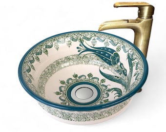 May include: A white ceramic sink with a blue and green floral design. The sink has a round shape and a drain in the center.