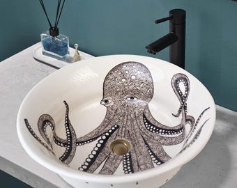 May include: White ceramic bathroom sink with an octopus design. The octopus is black and gray with a white background. The sink has a round shape and a drain in the center.