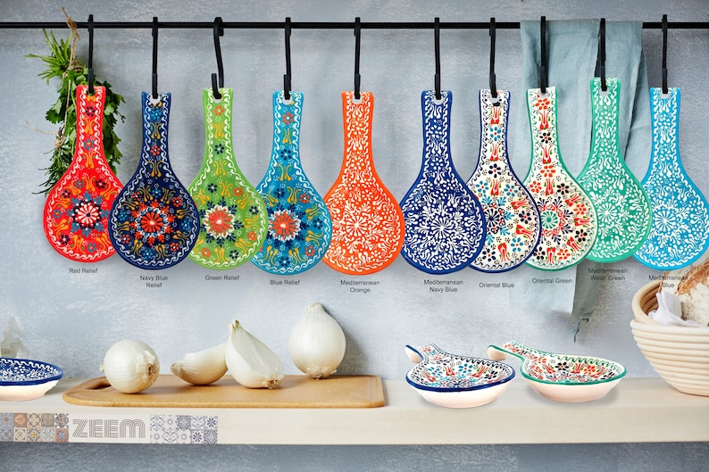 Pode incluir: Dez repousos de colher de cer&acirc;mica coloridos com padr&otilde;es florais pendurados em um rack de metal. Os repousos de colher s&atilde;o de v&aacute;rias cores, incluindo vermelho, azul, verde, laranja e turquesa. Os repousos de colher s&atilde;o etiquetados com seus nomes, como "Red Relief", "Navy Blue Relief" e "Oriental Blue".