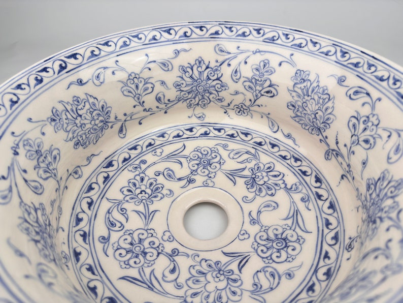 May include: A white ceramic sink with a blue and white floral pattern. The sink has a round shape and a drain hole in the center.