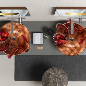 May include: Overhead view of a modern bathroom vanity with two round, brown glass sinks. Each sink features a red dragon sculpture. The vanity is grey, with a dark grey rug and a marble-topped side table.