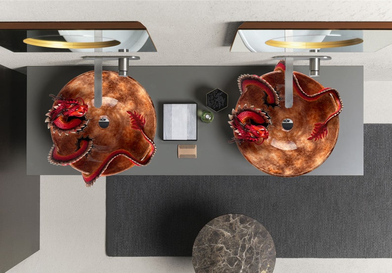 May include: Overhead view of a modern bathroom vanity with two round, brown glass sinks. Each sink features a red dragon sculpture. The vanity is grey, with a dark grey rug and a marble-topped side table.