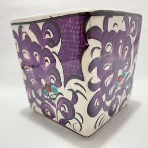 May include: Square ceramic planter with a purple and white floral design. The planter has a textured surface and is decorated with intricate details.