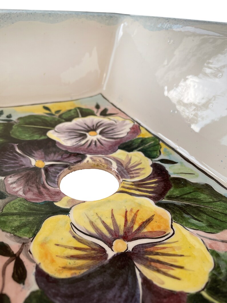 May include: A white ceramic sink with a square shape and a drain hole. The sink is decorated with hand-painted purple, yellow, and green pansies.