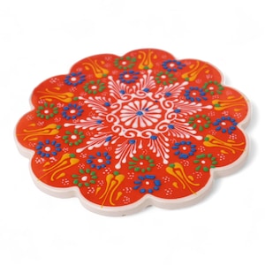 Könnte beinhalten: Ein roter Keramik-Untersetzer mit einem weißen und mehrfarbigen Blumenmuster. Der Untersetzer ist blumenförmig mit abgerundeten Kanten.