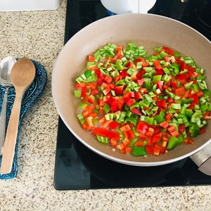 Pode incluir: Um close-up de uma panela com piment&otilde;es vermelhos e verdes picados cozinhando em &oacute;leo em um fog&atilde;o.
